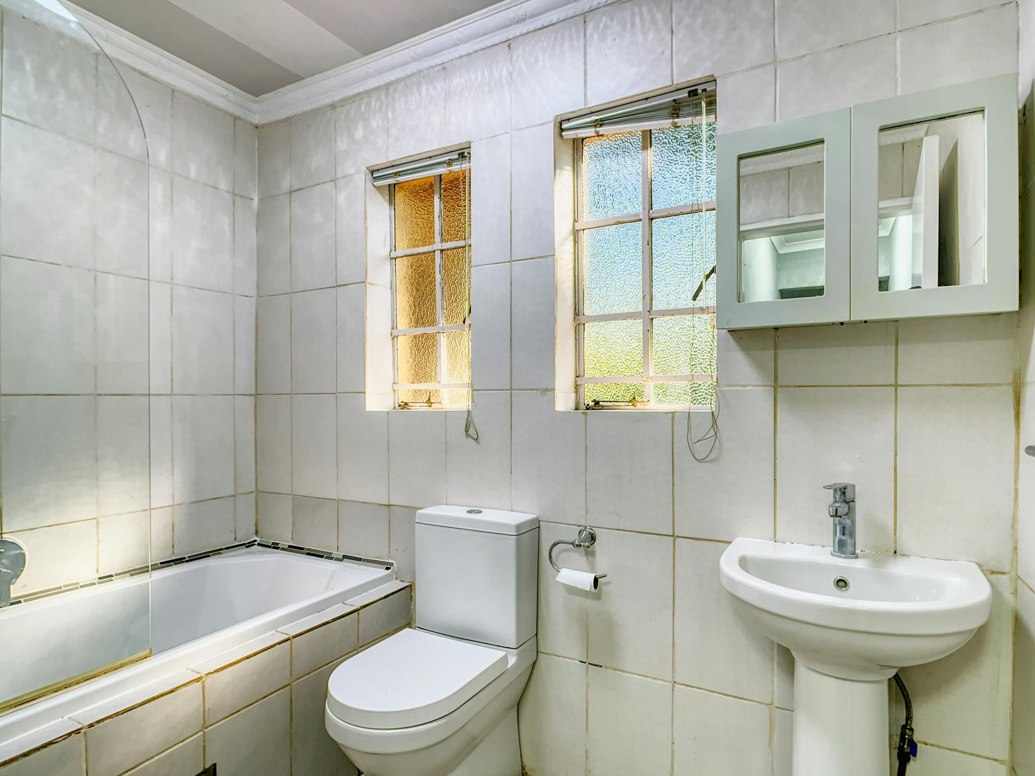 Bright and clean white bathroom with a bathtub, sink, toilet, and windows allowing natural light.