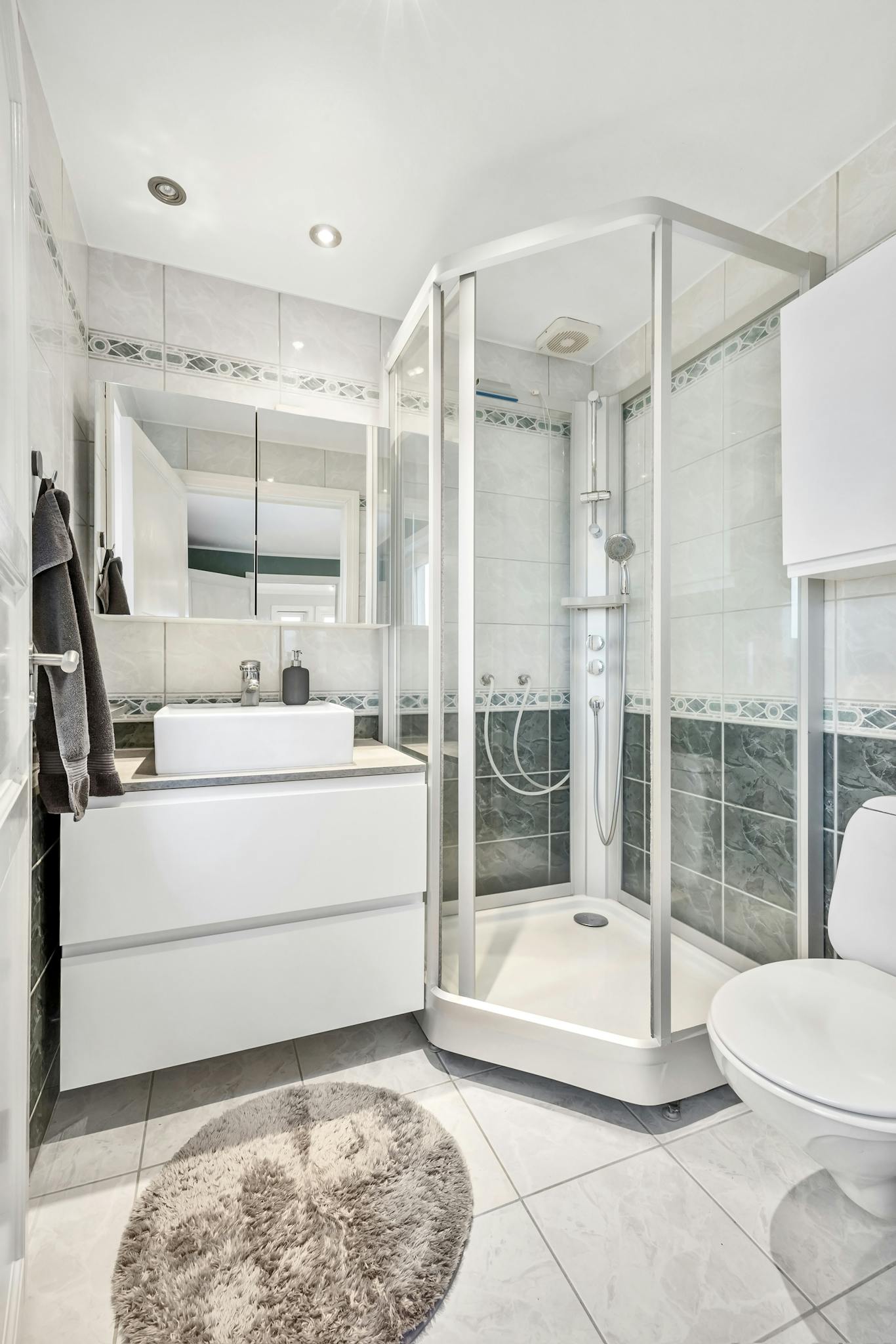 Elegant bathroom featuring a glass shower, modern white fixtures, and tile flooring, showcasing minimalistic and contemporary design.