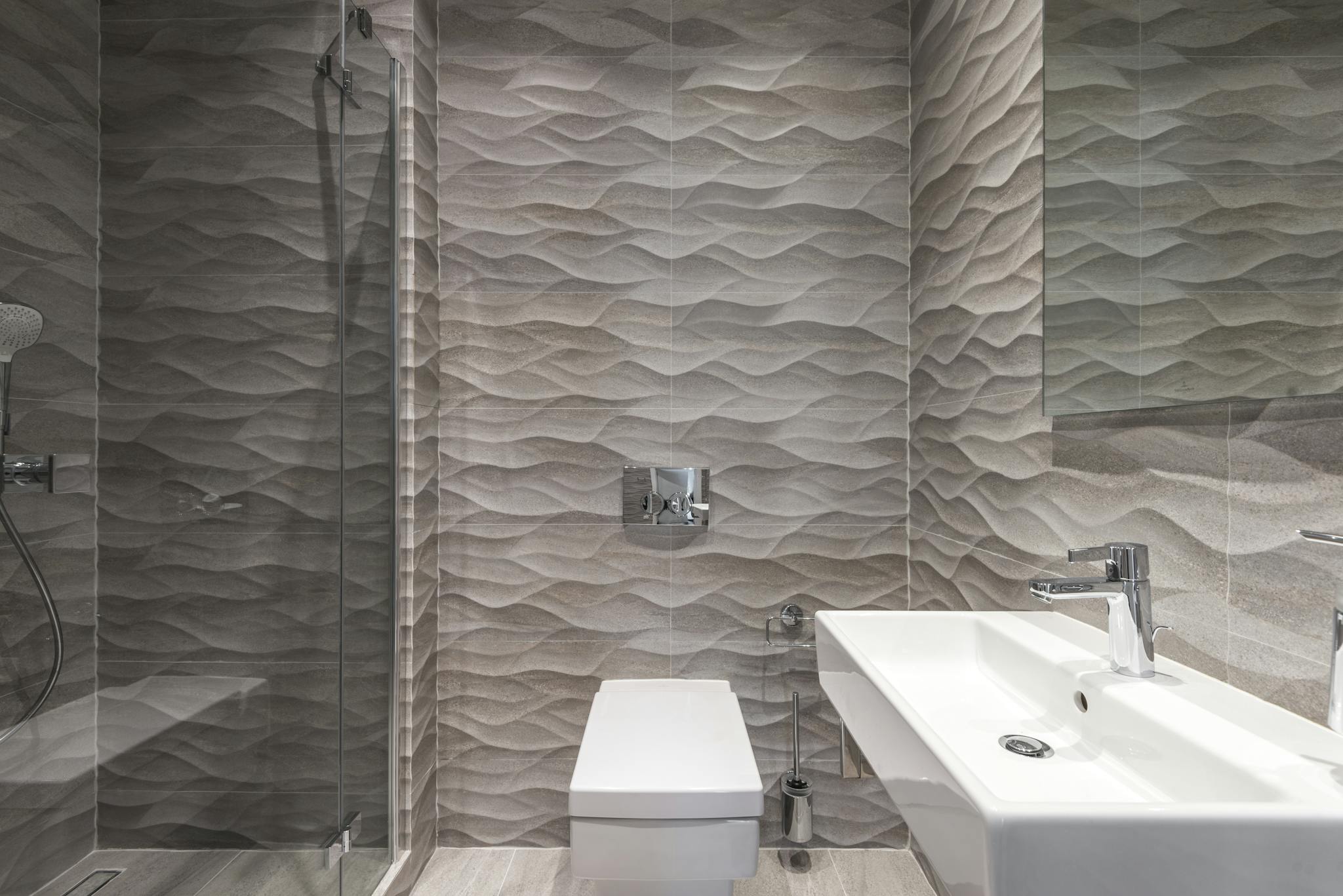 Sleek bathroom featuring textured walls, a glass shower, and a modern sink.